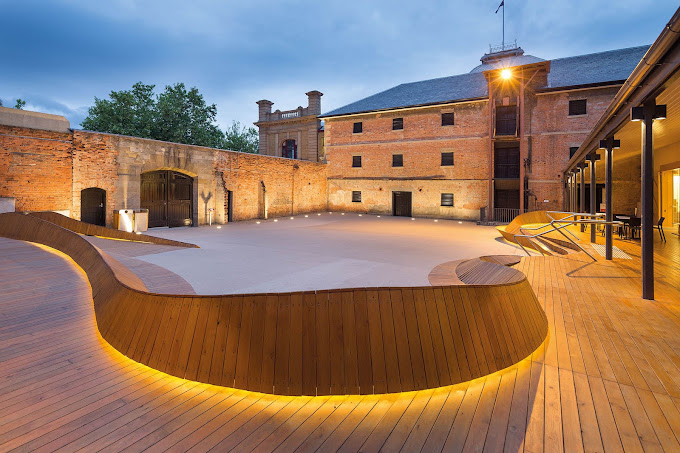 Historic sandstone courtyard of the Tasmanian Museum and Art Gallery lit up at dusk, with a curved timber deck