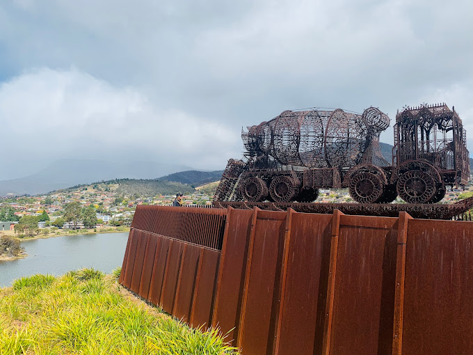 Large woven-metal sculpture of a cement-mixer truck perched on a rust-coloured wall at MONA, overlooking the Derwent River