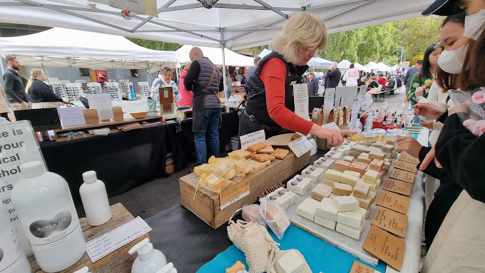 Stallholder arranging handmade soaps at a market stand under white marquees at Salamanca Market